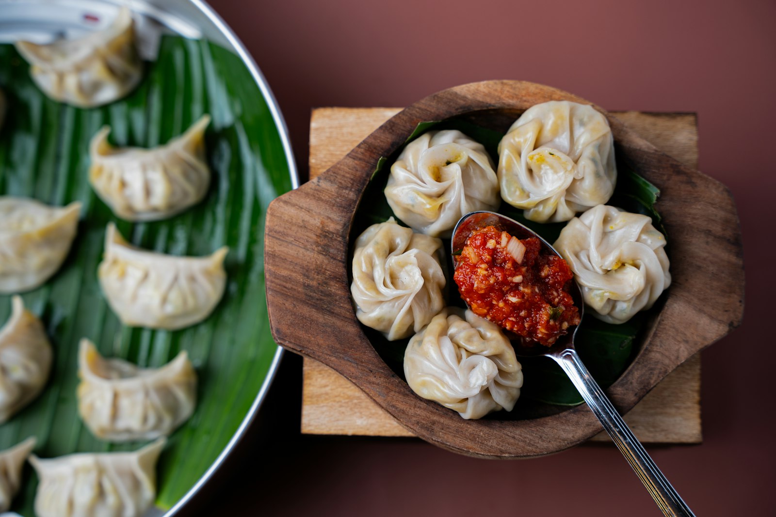 Steamed dumplings in a wooden bowl with chili sauce, photographed from above